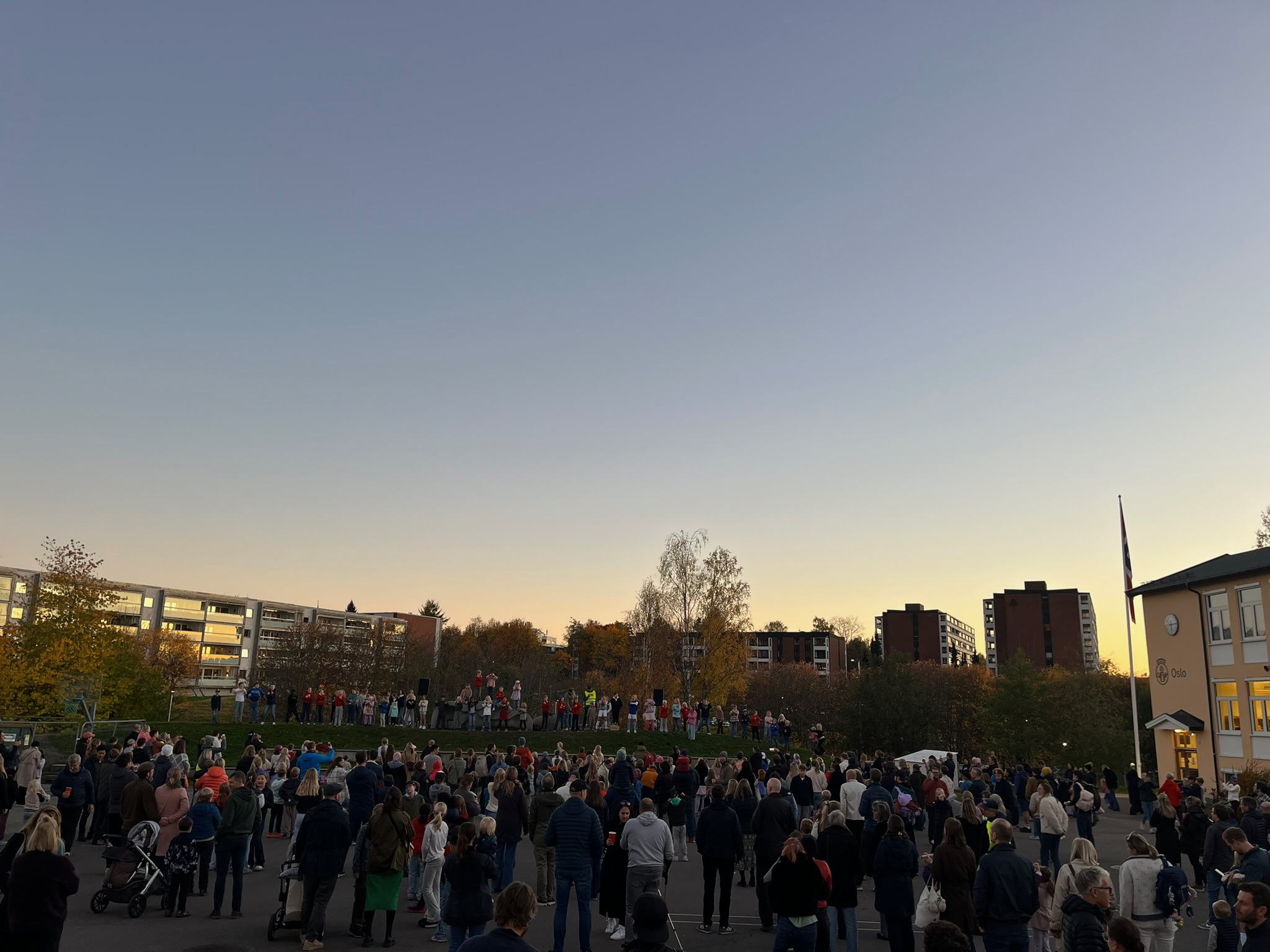 En mengde mennesker utenfor en skole i kveldsstemning